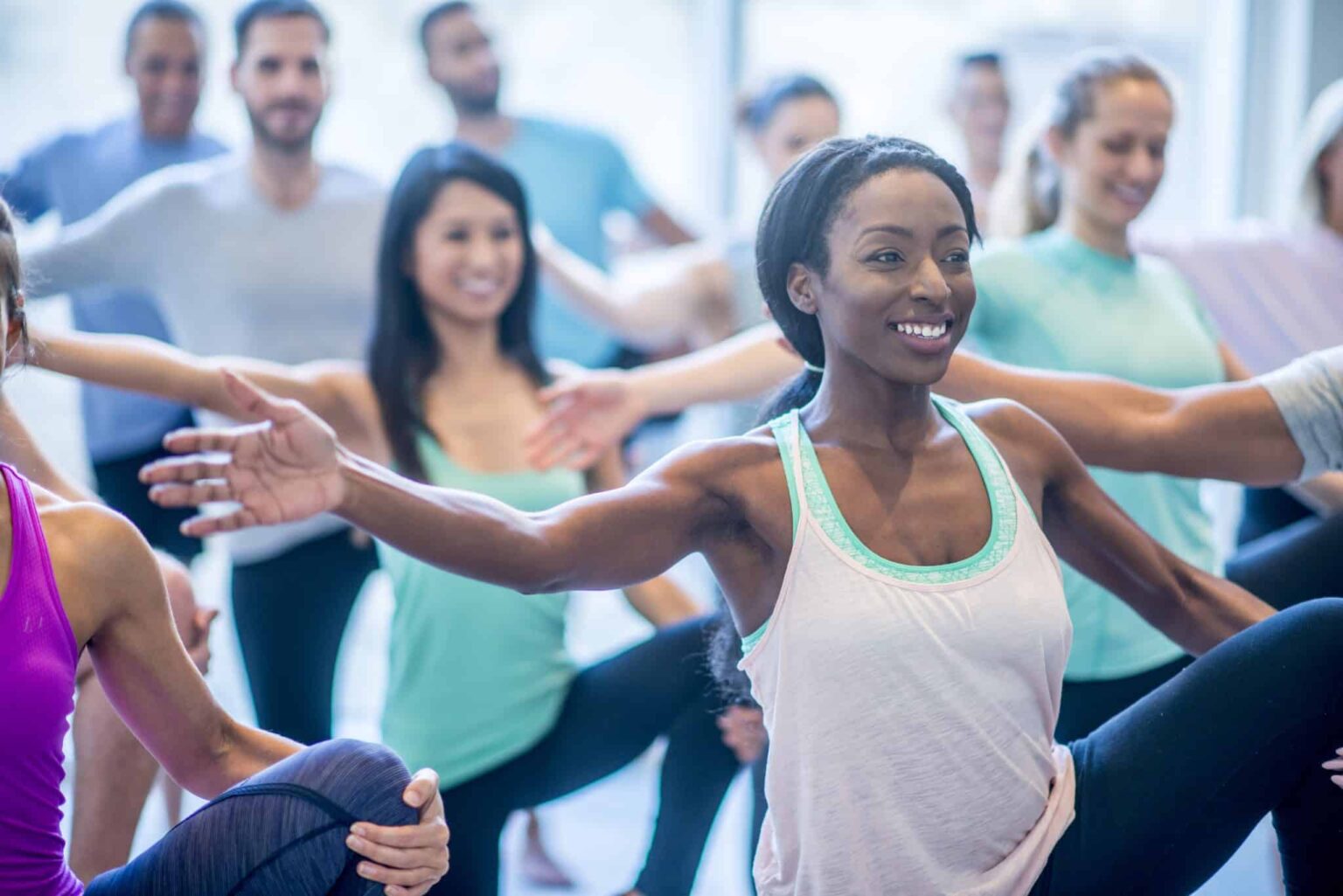 treatment results of balance testing Woman smiling in an exercise class with arm outstretched. She is balancing in a group class with men and woman. She is holding her knee with her hand.
